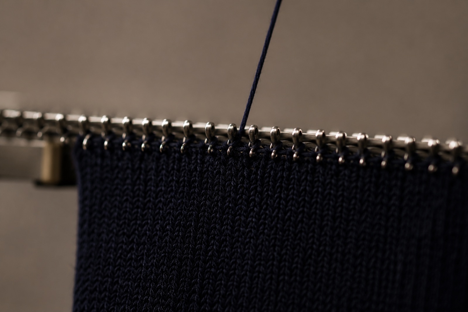 A navy knitted panel held on the points of a linking machine