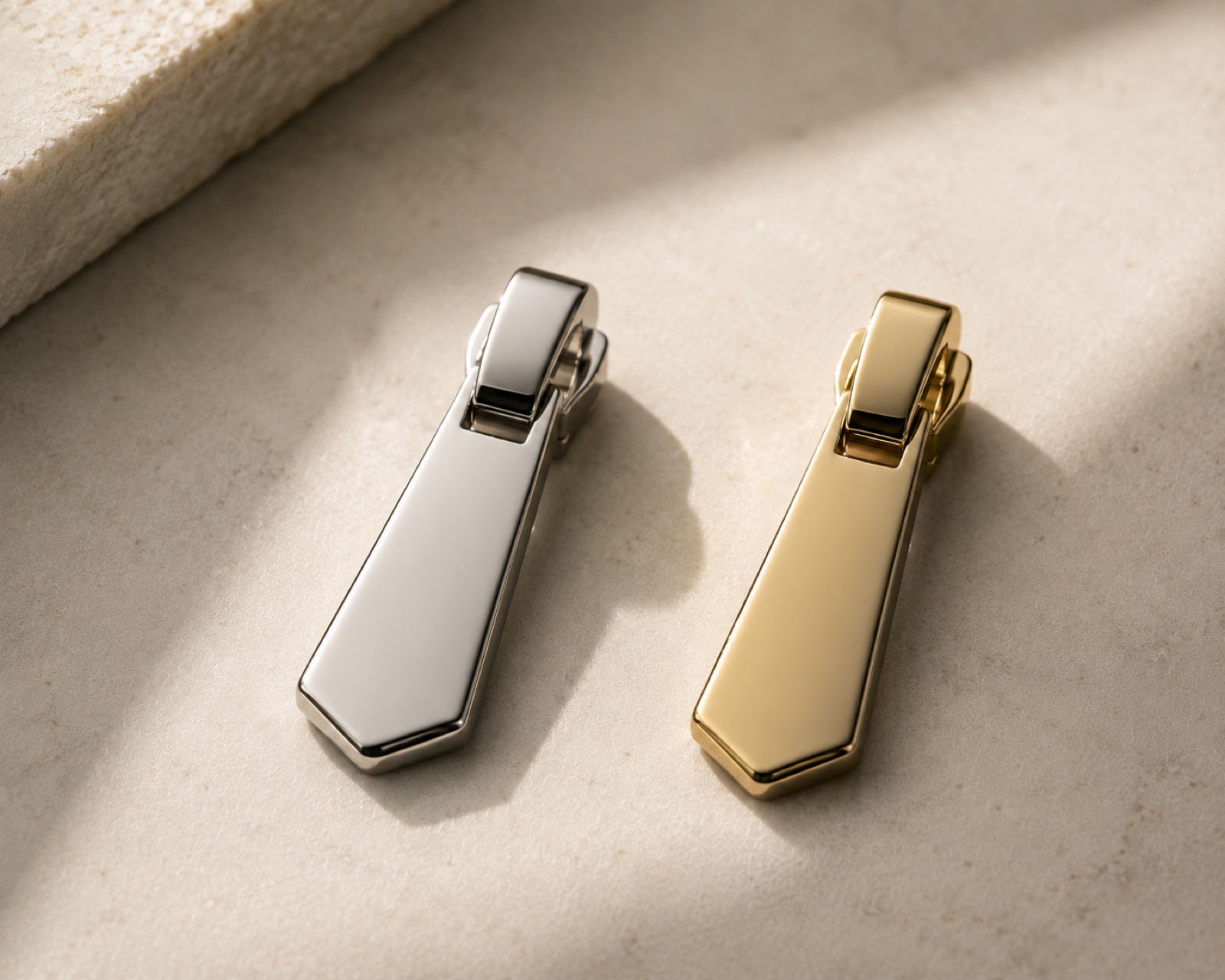 Two zip pulls, one palladium and one gold, on pale stone